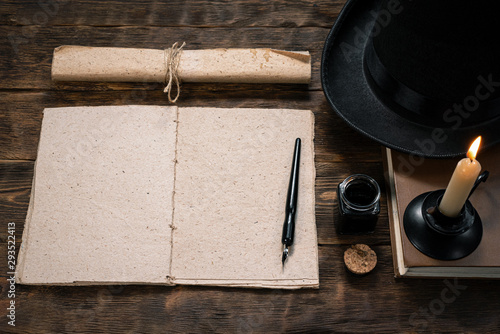 Open blank page book, old scroll, quill pen, bowler hat and burning candle on a writer wooden table background.