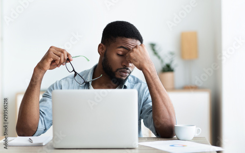 Tired african american employee having headache after working on laptop