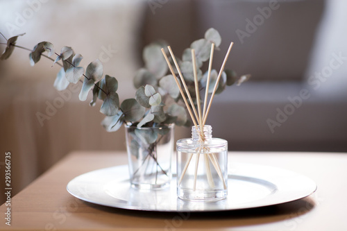 decoration, hygge and aromatherapy concept - aroma reed diffuser and branches of eucalyptus populus on table at home