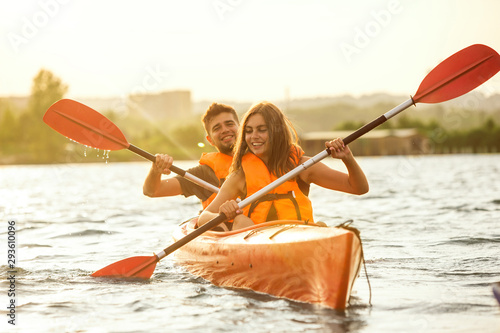 Happy young caucasian couple kayaking on river with sunset in the backgrounds. Having fun in leisure activity. Happy male and female model laughting on the kayak. Sport, relations concept. Colorful.