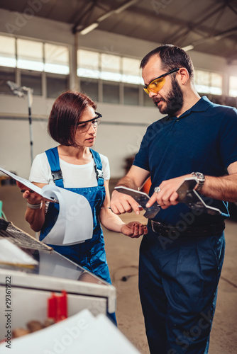 Female CNC Machine Operator and supervisor measuring cut out product