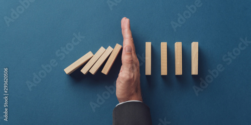 Business crisis manager stopping falling dominos from collapsing