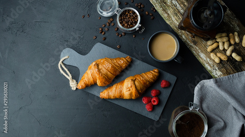 Rogale croissant leżące na ciemnej desce w otoczeniu malin i kawy. Ciemne tło, widok z góry.