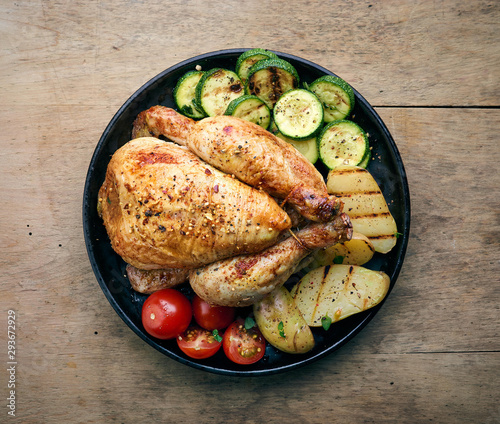 Roasted whole chicken with grilled vegetables on black plate