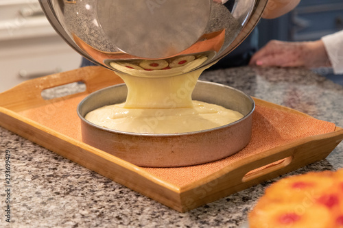 Cake batter being poured out of a silver bowl into a round cake pan