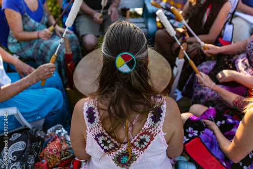 Sacred drums during spiritual singing. A high angle view of a woman wearing native headband and colorful clothes during a singing circle of people around a sacred mother drum outdoors.