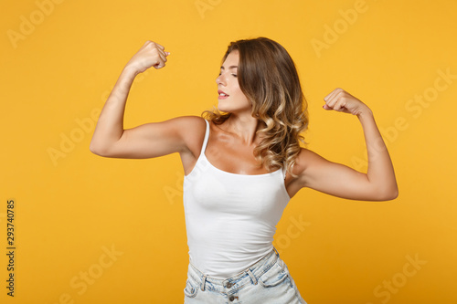 Strong young woman girl in light casual clothes posing isolated on yellow orange wall background studio portrait. People sincere emotions lifestyle concept. Mock up copy space. Showing biceps muscles.
