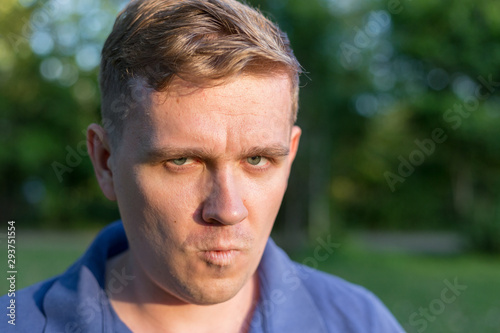Man with a scornful disdainful disrespectful look. Portrait of a young guy on nature background, feelings and people reaction. Anger rage and hatred