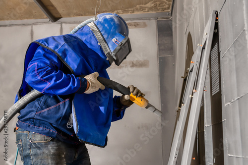 The operator of the sandblasting machine is ready to go. The worker is wearing a safety helmet and mask.