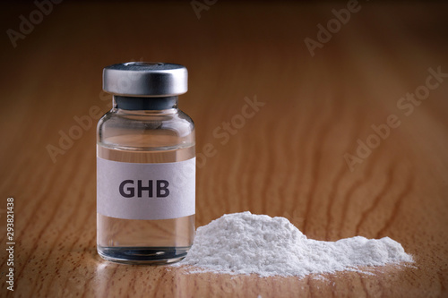 Bottle of GHB with drug powder on wooden background.GHB