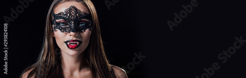 panoramic shot of naked scary vampire girl in masquerade mask showing fangs isolated on black