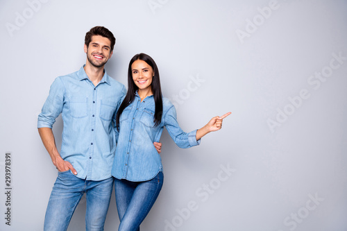 Photo of cheerful trendy charming brown haired nice cute couple of two people pointing at emptiness away wearing jeans denim jackets isolated over grey color white background