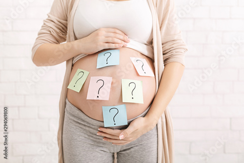 Confused pregnant woman with question marks on paper stickers on tummy