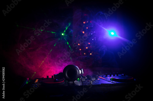 Dj mixer with headphones on dark nightclub background with Christmas tree New Year Eve. Close up view of New Year elements on a Dj table. Holiday party concept.