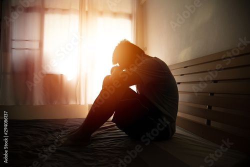 desperate man in silhouette sitting on the bed with hands on head