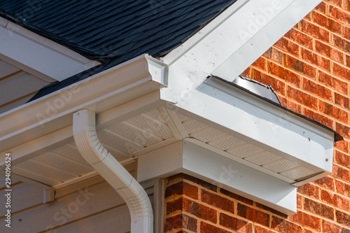 Gable with brick and vinyl siding, white frame gutter guard system, fascia, drip edge, soffit, on a pitched roof attic at a luxury American single family home neighborhood USA