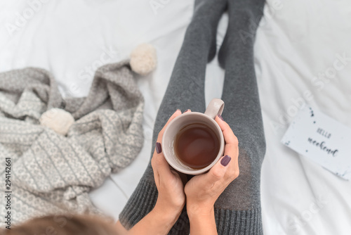 Woman`s legs in leg warmers in bed. Beautiful girl sitting in her bed and drinking morning tea