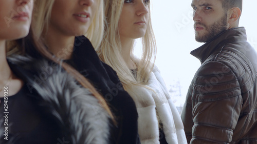 A young bearded man looks at three women in expensive furs and turns away from them. Family concept mistresses and macho.
