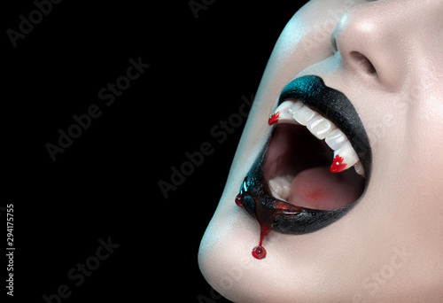 Vampire teeth with dripping blood, Woman's black bloody lips close-up. Vampire girl fangs. Fashion Halloween art design. Close up of female vampire mouth, teeth. Isolated On black background