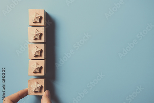 Man Hand putting wooden five star shape on blue background. Best Excellent Services Rating for Satisfaction.