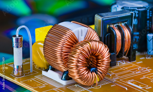 Toroidal inductors with copper wire winding, transformer and electric fuse. Electronic components on circuit board detail from dismantled power supply unit. Induction coils on blue colored background.