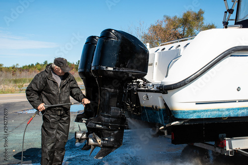 Caucasian man pressure washing outboard motors on power boat