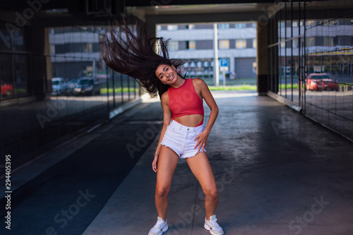 Young brunette woman dancing and shaking her hair in arch of building.
