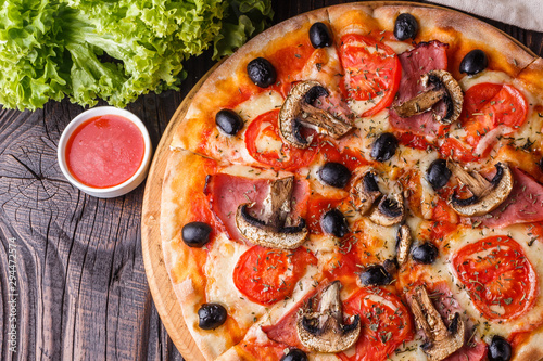 Pizza with tomato, olives, champignons, ham and cheese on round wooden plate