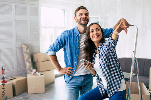 The planning process. Appealing couple of a young woman with dark wavy hair and her husband are planning furnishing and design of their new flat.