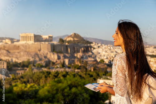 Touristin mit Reiseführer in der Hand schaut auf den Parthenon Tempel der Akropolis von Athen, Griechenland, bei Sonnenuntergang im Sommer