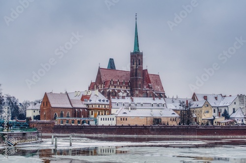 zimowy krajobraz Wrocławia stolicy Śląska, rzeka Odra wyjątkowo skuta lodem, widok na Ostrów Tumski z gotyckim kościołem Świętego Krzyża