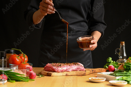 Chef cooks pork steak. pouring sauce, marinade on a background with vegetables. Recipe book, cooking, restaurant business