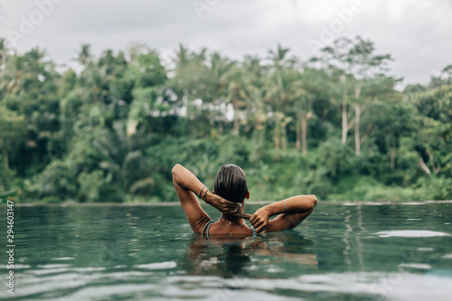 Woman enjoying tropical rain while swimming in infinity pool on Bali