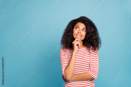 Photo of serious confused interested black millennial trying to remember important information biting her lips touching chin with hands isolated over blue color vivid background