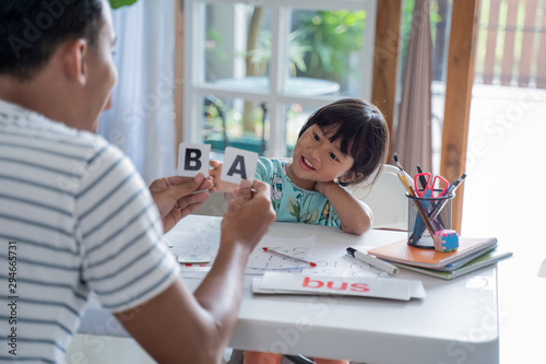 portrait of father teaching toddler how to read by using simple word and letter on a flash card at home