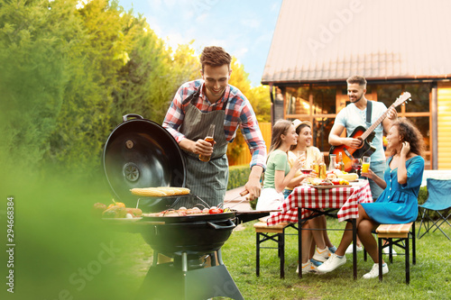 Group of friends at barbecue party outdoors. Young man near grill
