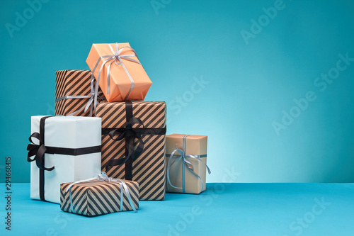 Different sizes, colorful, striped and plain paper gift boxes tied with ribbons and bows on a blue surface and background. Close-up, copy space.