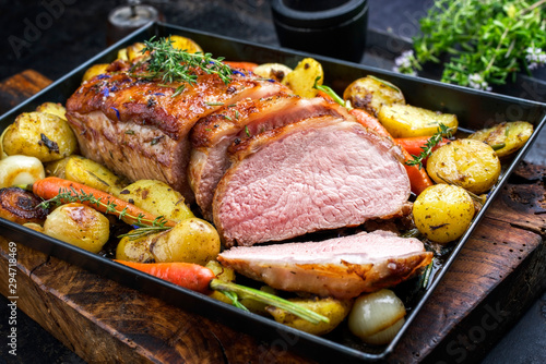 Traditional roasted dry aged veal tenderloin with carrots and potatoes offered as closeup on a metal tray