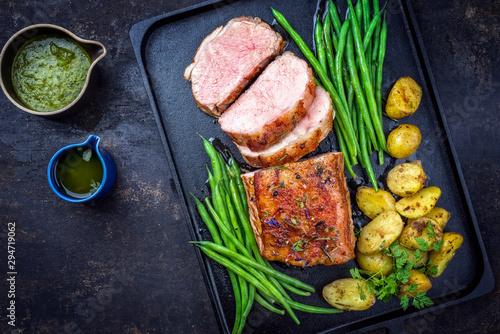 Traditional roasted dry aged veal tenderloin with beans and potatoes offered as top view on a modern design cast iron tray