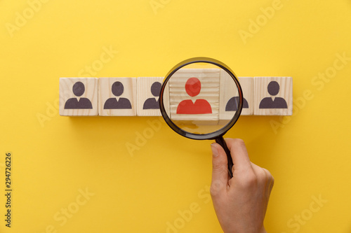 cropped view of woman holding magnifying glass under wooden cubes with logo on yellow background
