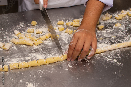 Chef making a potato gnocchi pasta. Showing only his hands, on a stainless steel floured worktop. Your hands are dirty with flour.