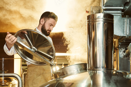 Brewer looking in metallic brew kettle with steam.