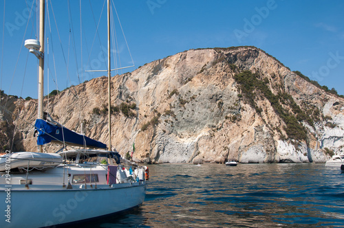 A sailboat near a cliff. The rocky cliff of the island of Ponza in the summer.