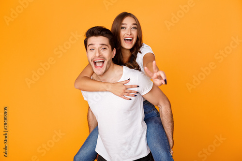 Young man giving piggyback ride to woman, showing peace sign