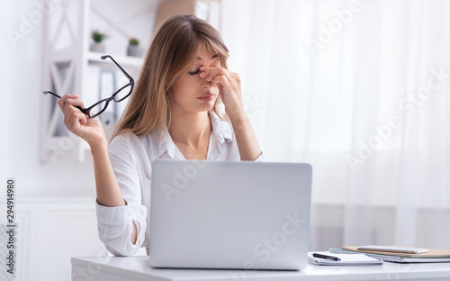 Overworked Girl Massaging Nosebridge Sitting At Laptop At Workplace