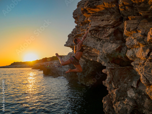 SUN FLARE: Strong girl climbs a challenging cliff on a sunny summer evening.