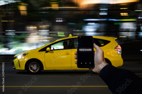 A cell phone with the the words rideshare on the screen on in front of a yellow taxi in the background.