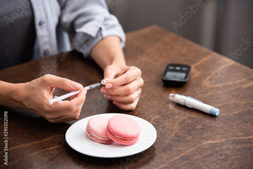 cropped view of woman holding syringe near sweet dessert and blood lancet