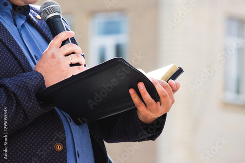 A preacher with a microphone in his hand holds a Bible and reads a passage from it_