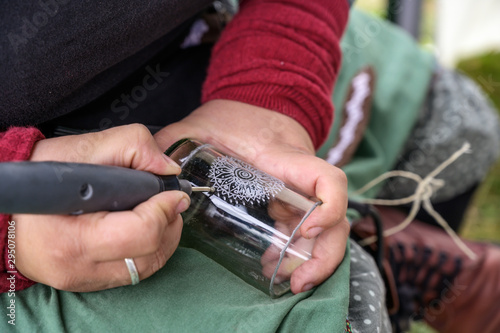 hands of a woman engraving a decorative pattern into a glass vase from a recycled bottle at a craft market